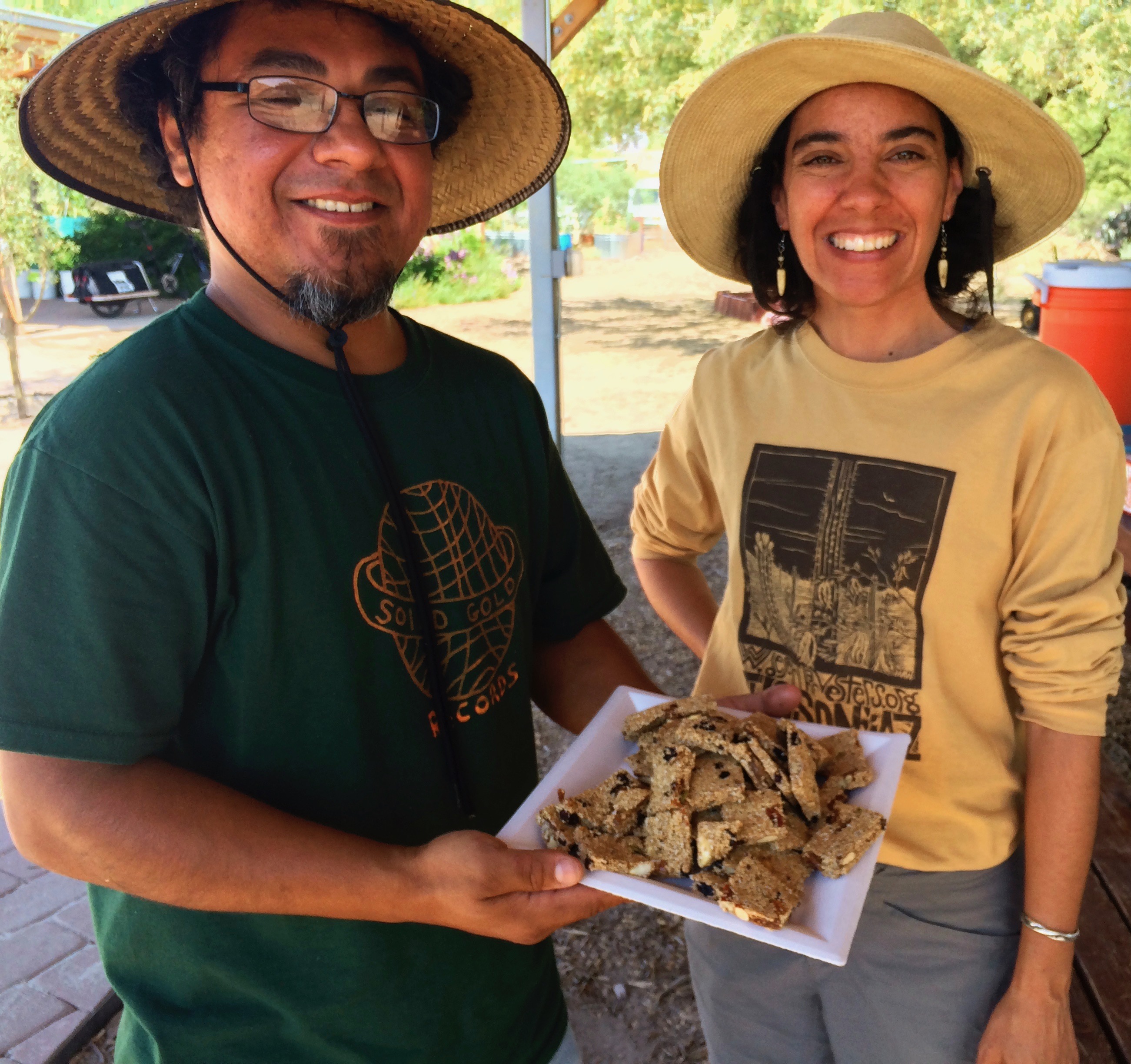 man in sunhat holding plate with delicious alegria bars next to smiling Desert Harvesters volunteer